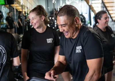 Group fitness class at Shred Shed, with members laughing and training together inside the gym while wearing Shred Shed workout shirts.